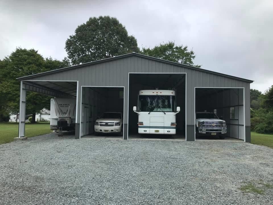 Gray custom barn with RV and vehicles parked in four spaces.