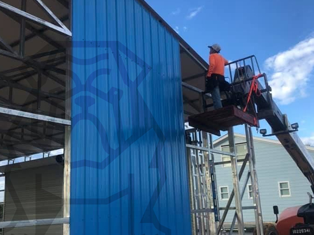 worker installing blue metal siding on a building