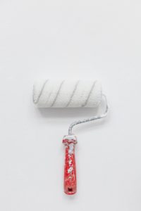 Small paint roller with white paint. Red handle.