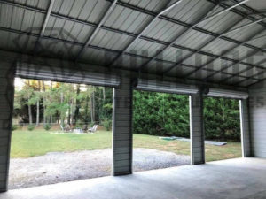 View of outdoors from inside a steel structure with three garage door openings.